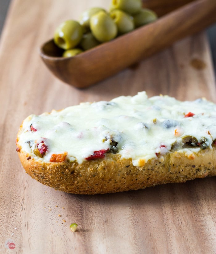 Toasty French Bread is topped with my New Orleans Olive Salad and covered with cheese. Cheesy Olive Salad Bread | Take Two Tapas | #OliveBread #CheesyOliveBread #CheeseBread #Appetizers