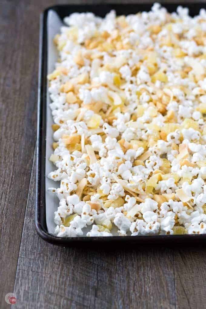 A tropical snack mix of dried pineapple, toasted coconut chips, roasted macadamia nuts, drizzled in white chocolate. Perfect for a slightly healthier popcorn snack mix for those days when you are craving everything! Hawaiian Popcorn Mix Recipe | Take Two Tapas | #Popcorn #Hawaiian #PopcornSnack #HealthySnacks #TrailMix #HealthyPopcornRecipe