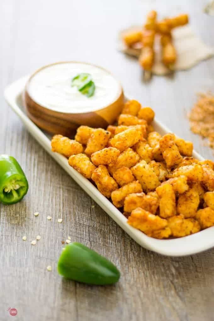 Steakhouse tater tots and jalapeno ranch dip in a wood bowl all on a white platter.