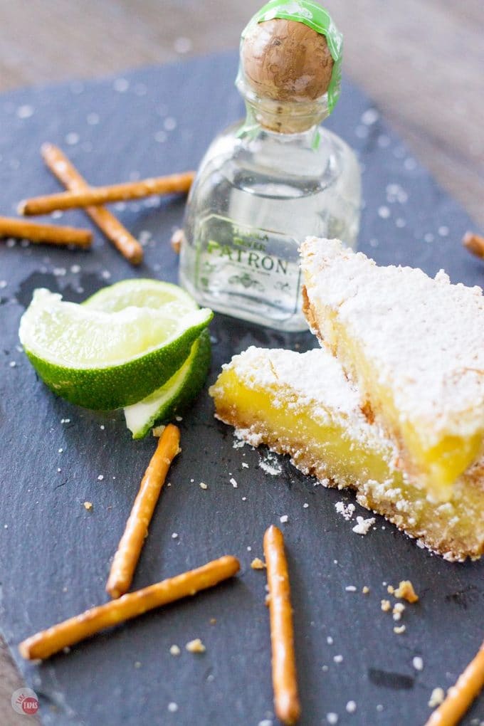 My favorite cocktail is now a dessert bar. Margarita Bars have a creamy and tart lime filling complete with a splash of tequila that sits atop a shortbread salty pretzel crust. A crispy top dusted with powdered sugar finishes off of this amazing dessert. Margarita Bars Recipe | Take Two Tapas | #MargaritaBars #Margarita #LemonBars #CincoDeMayo