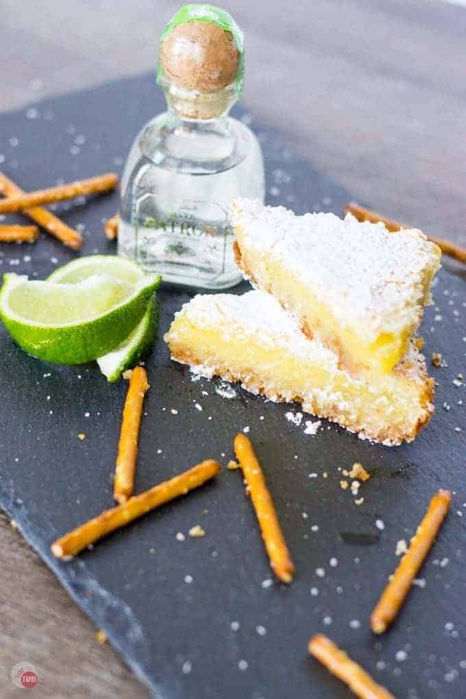 My favorite cocktail is now a dessert bar. Margarita Bars have a creamy and tart lime filling complete with a splash of tequila that sits atop a shortbread salty pretzel crust. A crispy top dusted with powdered sugar finishes off of this amazing dessert. Margarita Bars Recipe | Take Two Tapas | #MargaritaBars #Margarita #LemonBars #CincoDeMayo