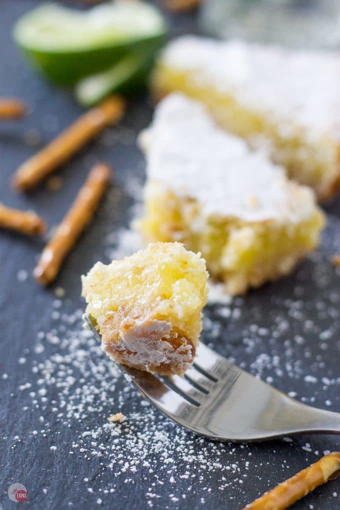 My favorite cocktail is now a dessert bar. Margarita Bars have a creamy and tart lime filling complete with a splash of tequila that sits atop a shortbread salty pretzel crust. A crispy top dusted with powdered sugar finishes off of this amazing dessert. Margarita Bars Recipe | Take Two Tapas | #MargaritaBars #Margarita #LemonBars #CincoDeMayo