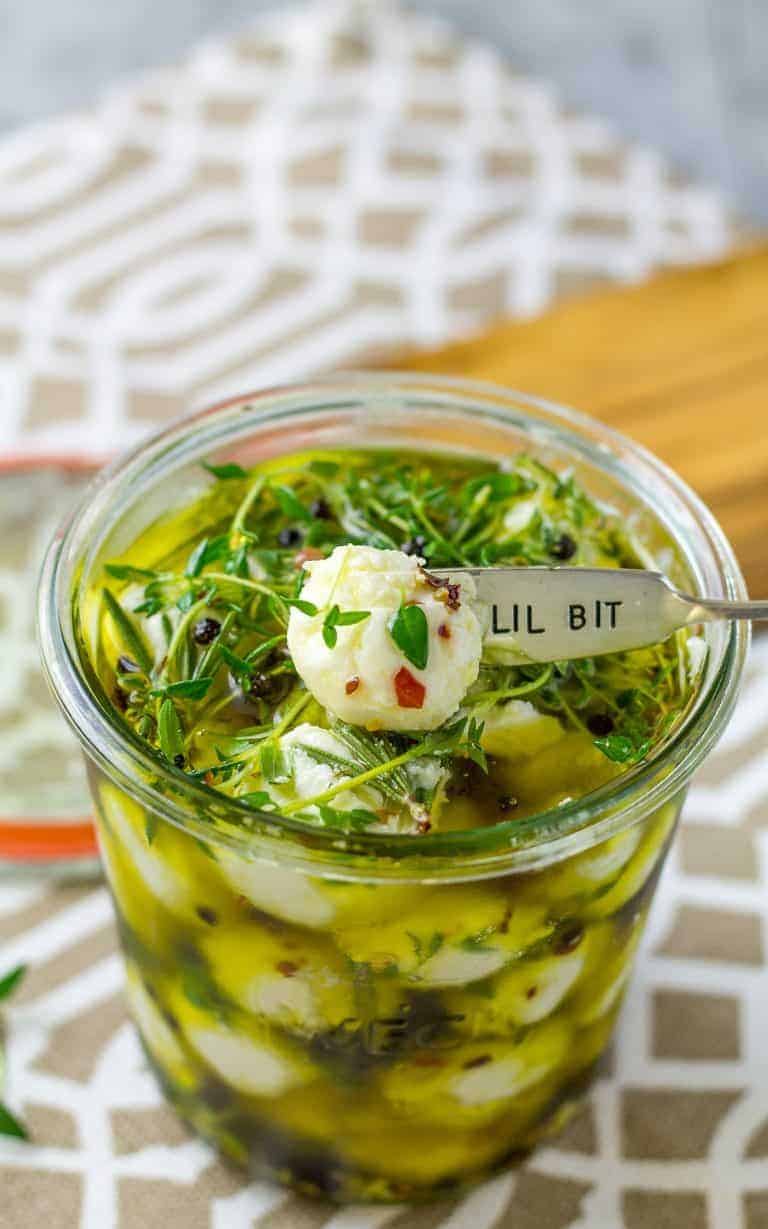 overhead of Herb Marinated Goat Cheese Balls in a glass jar sitting on a brown and white placemat