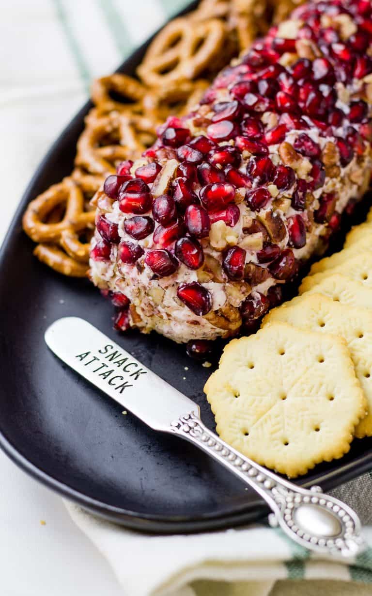 Close up of Pomegranate Drunken Goat Cheese Log, crackers and pretzels on a black platter.