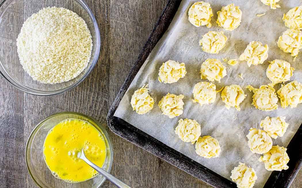 bevroren mac en kaasballetjes op een bakplaat met een kom panko en een kom losgeklopt ei