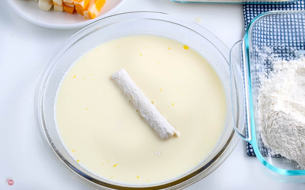 flour coated cheese stick in a bowl of milk