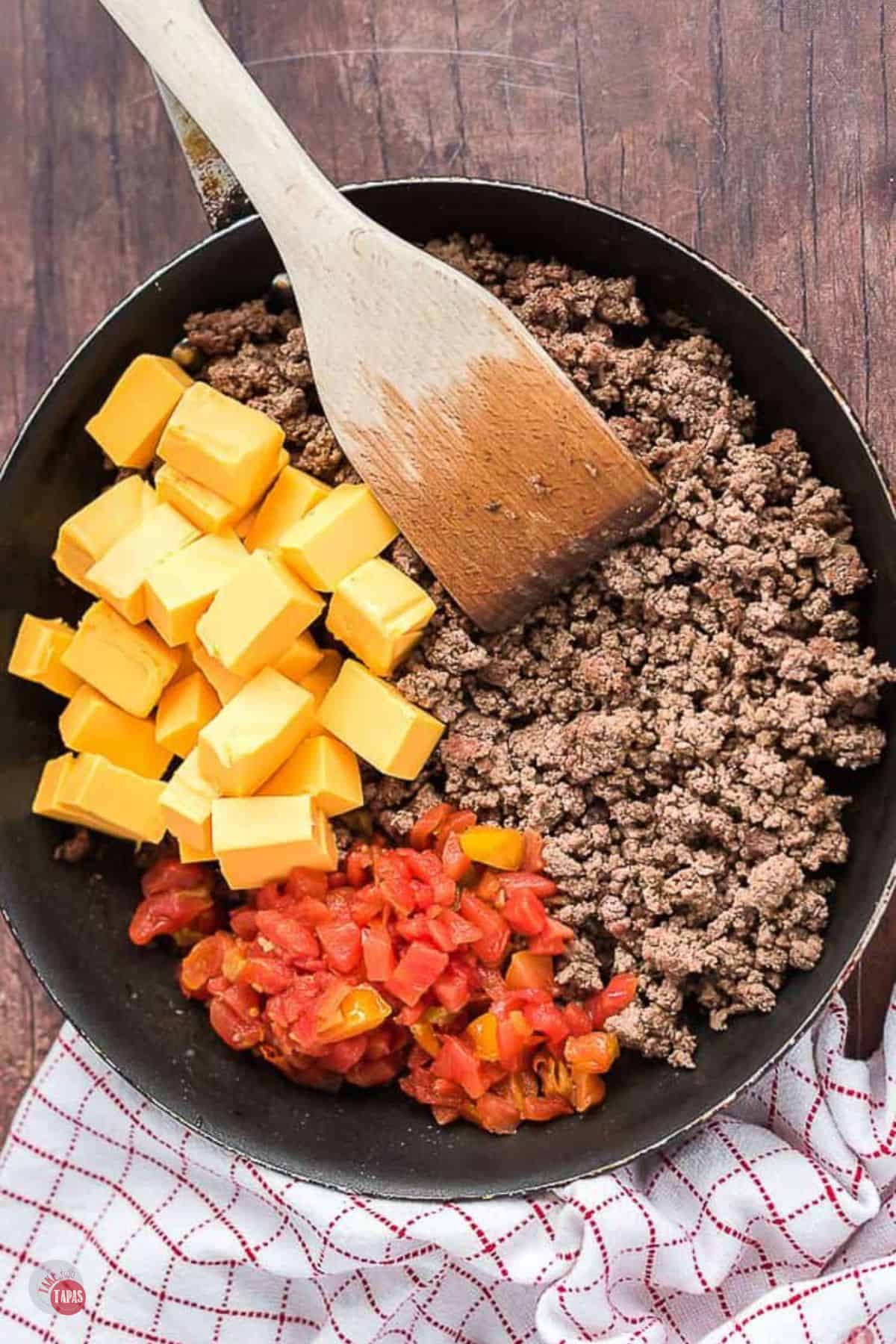 ground beef and cheese in a skillet with a wood spatula