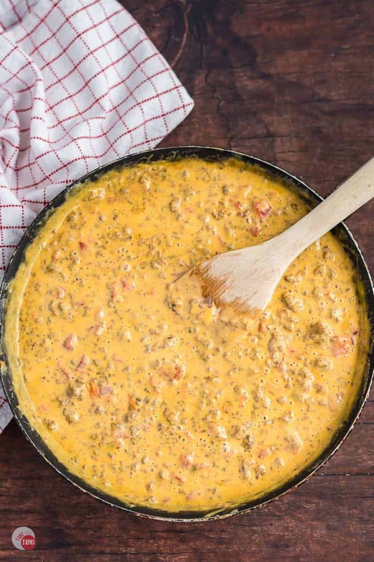 cheese dip in a pan being stirred with a wood spoon