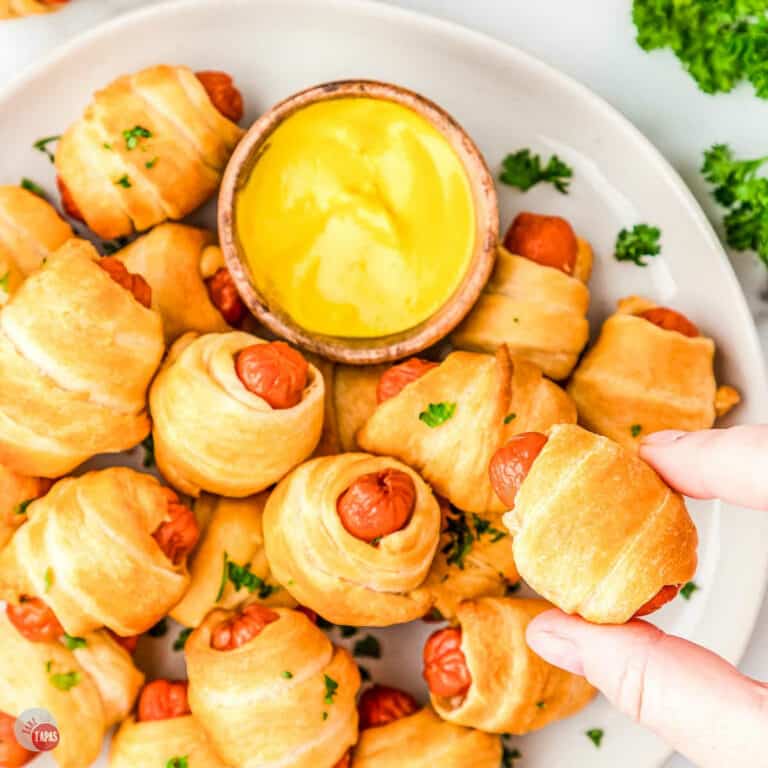 hand holding a pig in a blanket over a platter of them