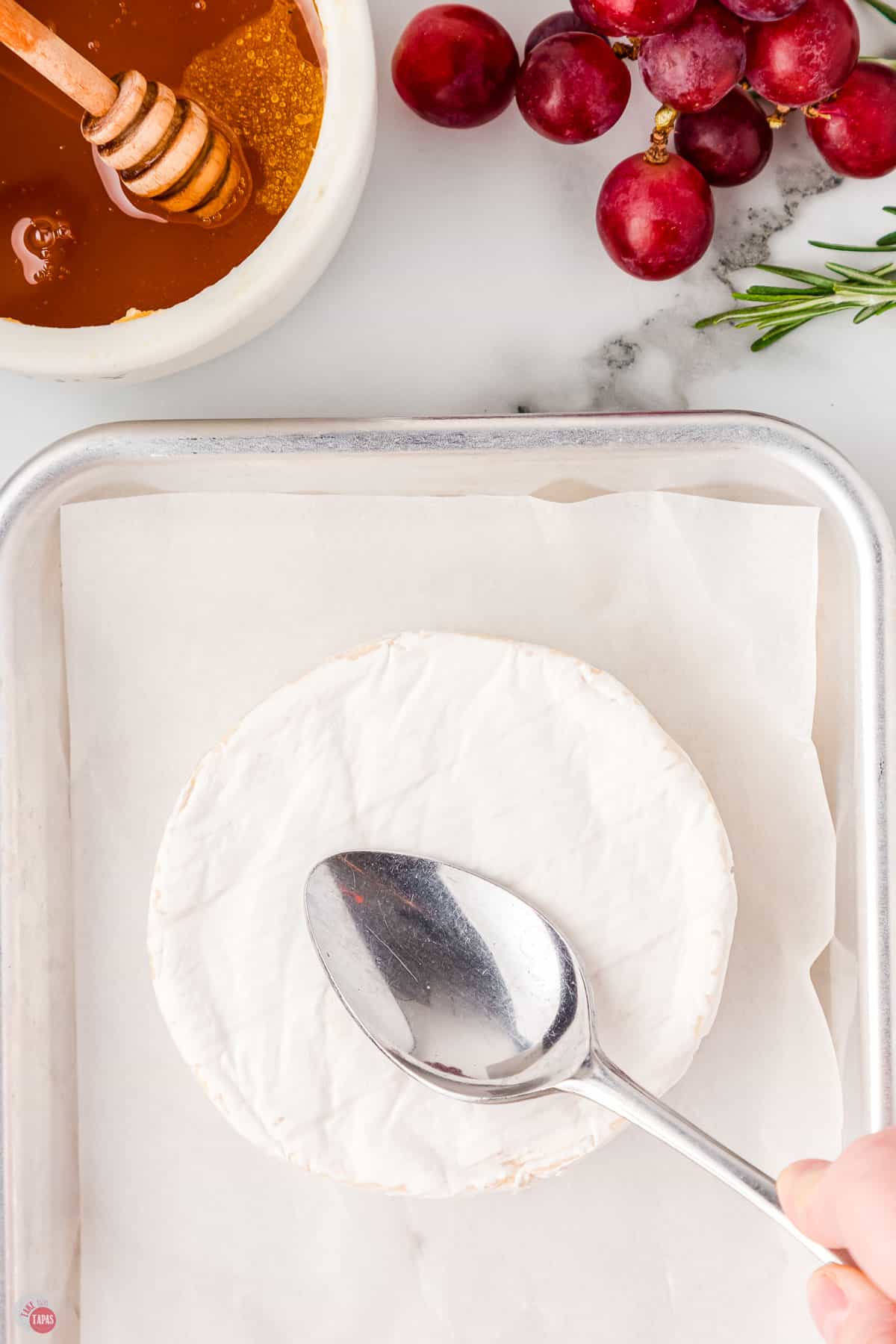 wheel of brie on a baking sheet with a spoon