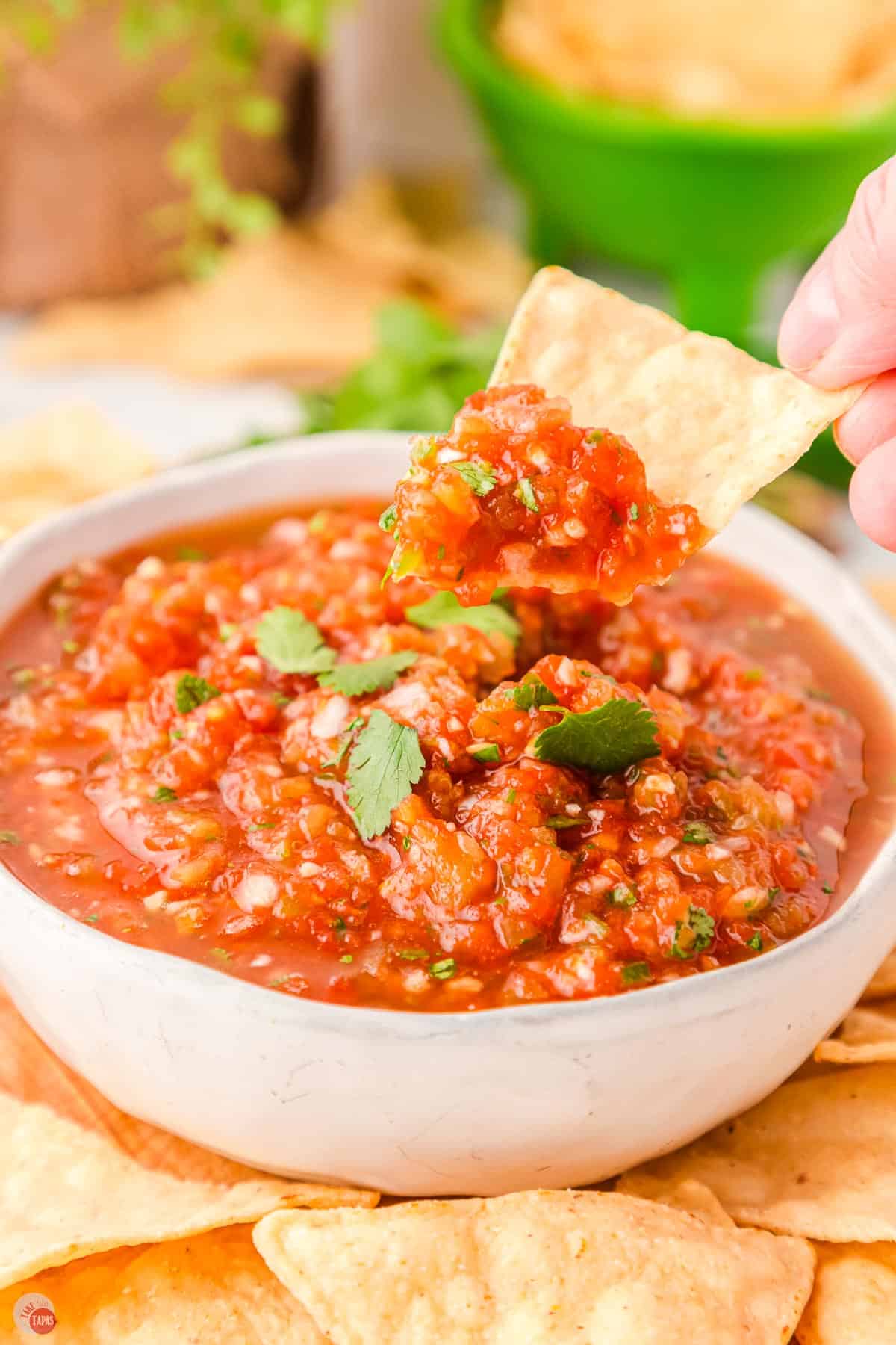 hand scooping out homemade salsa from a white bowl