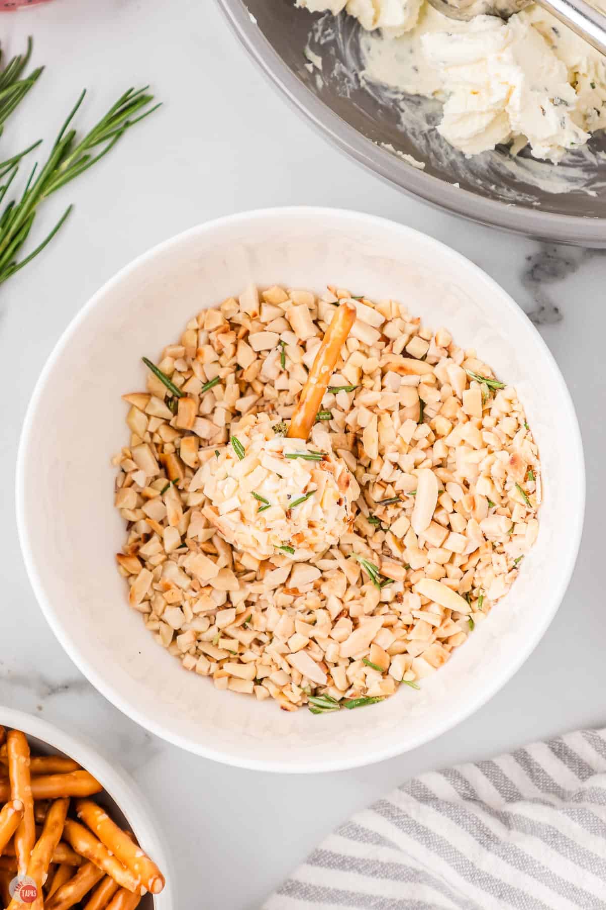 cheese ball covered in nuts in a bowl with a pretzel stick in it