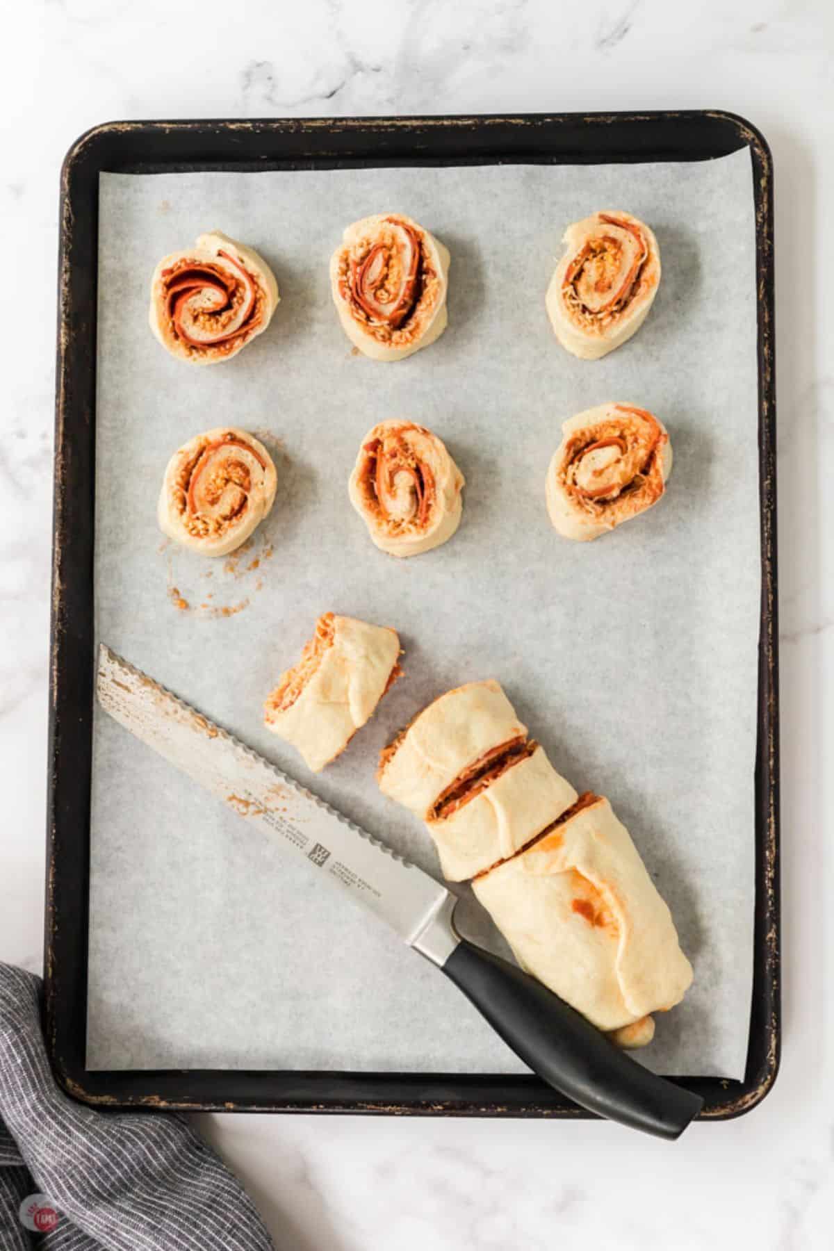 unbaked pinwheels on a baking sheet with a knife