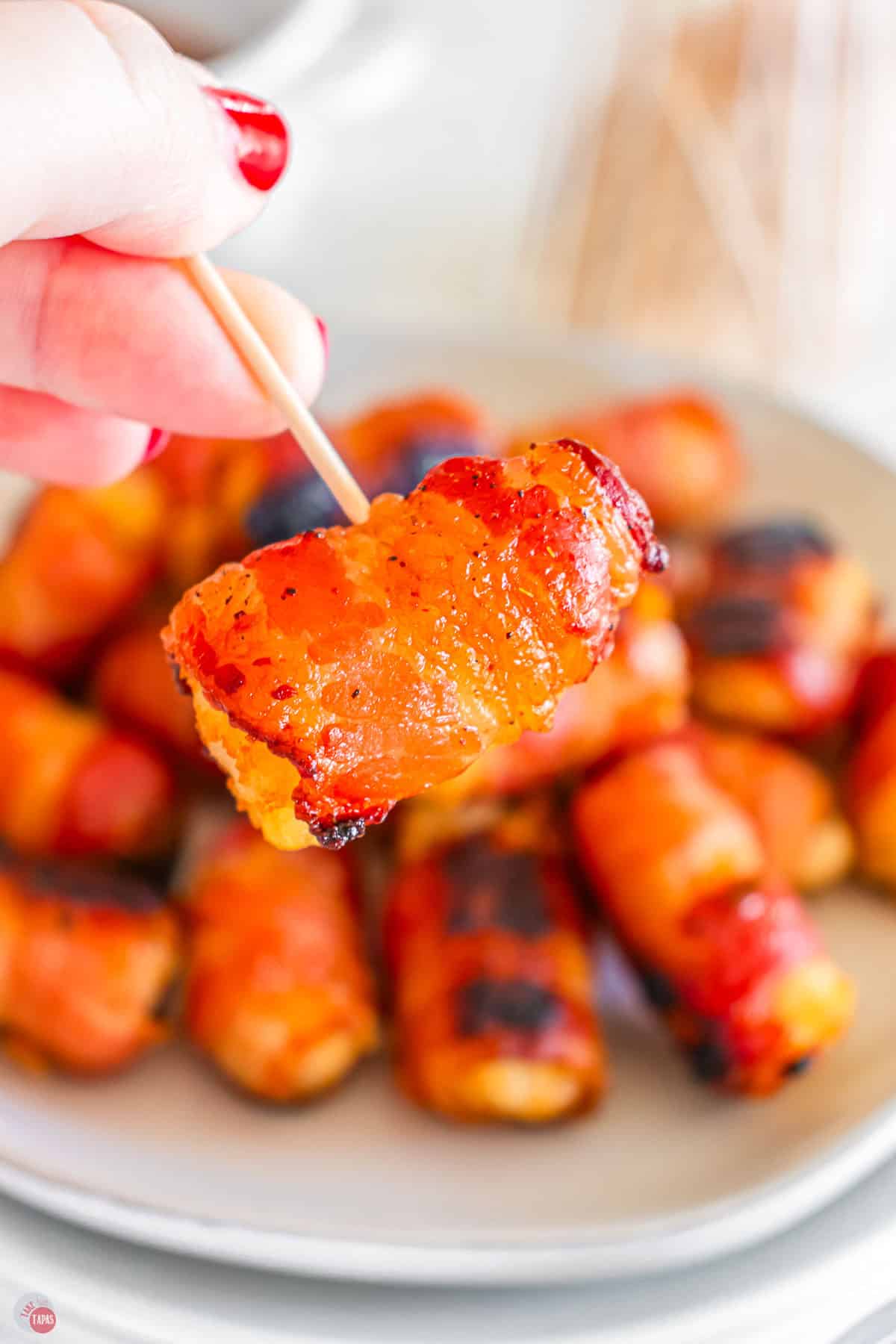 hand holding a toothpick with bacon and a tater tot