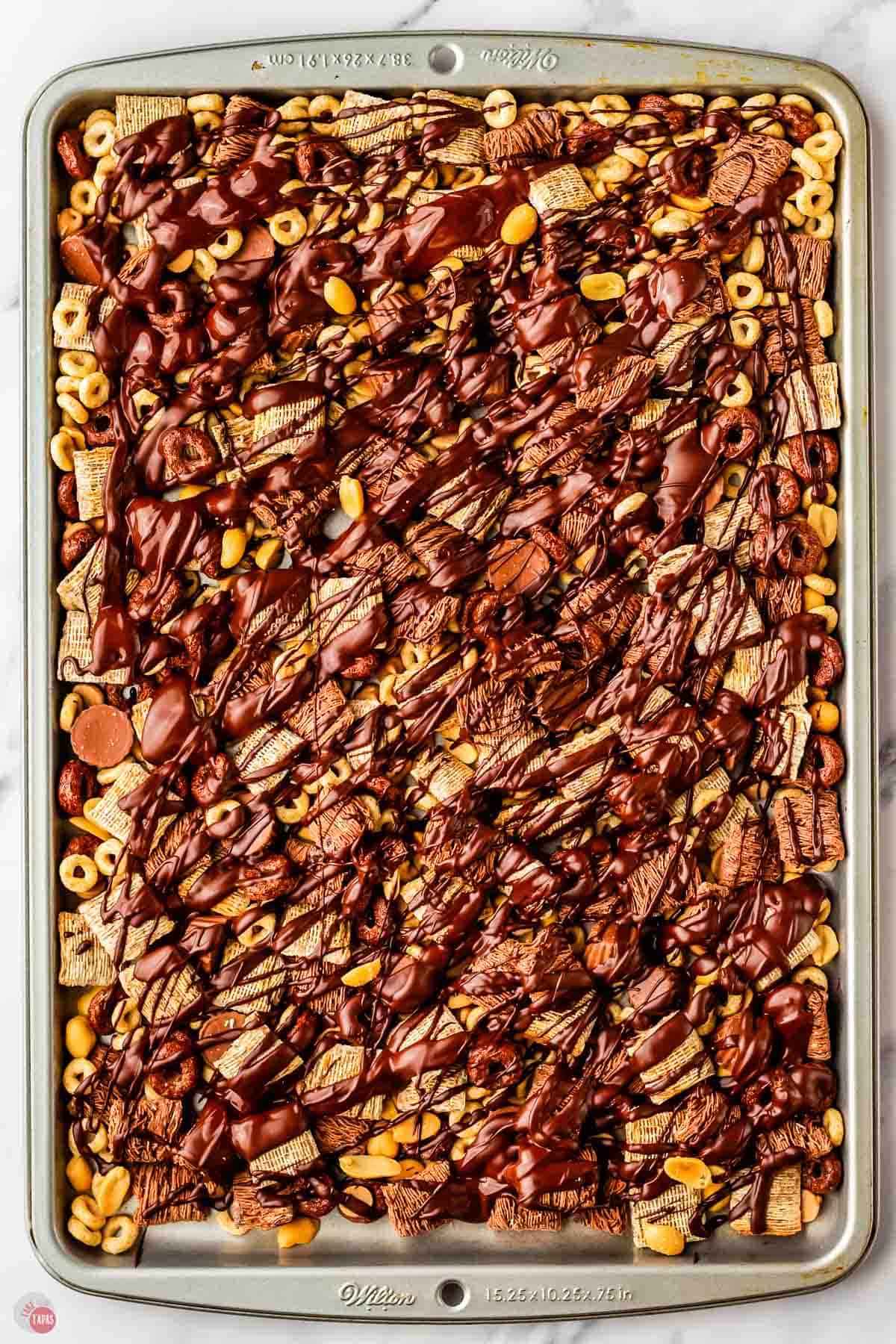 snack mix drizzled with chocolate on a cookie sheet