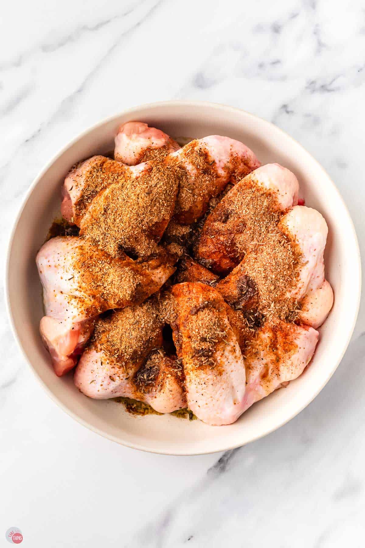 raw chicken pieces in a bowl sprinkled with spices