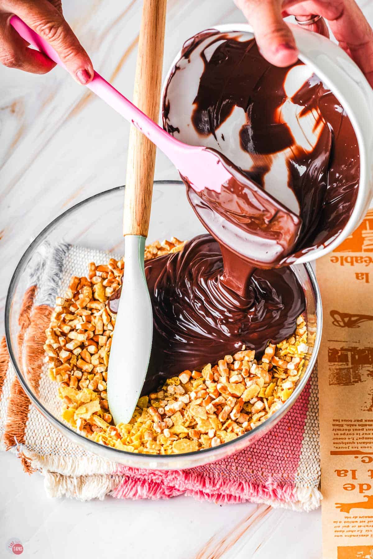 melted chocolate being poured into a bowl of crushed snacks