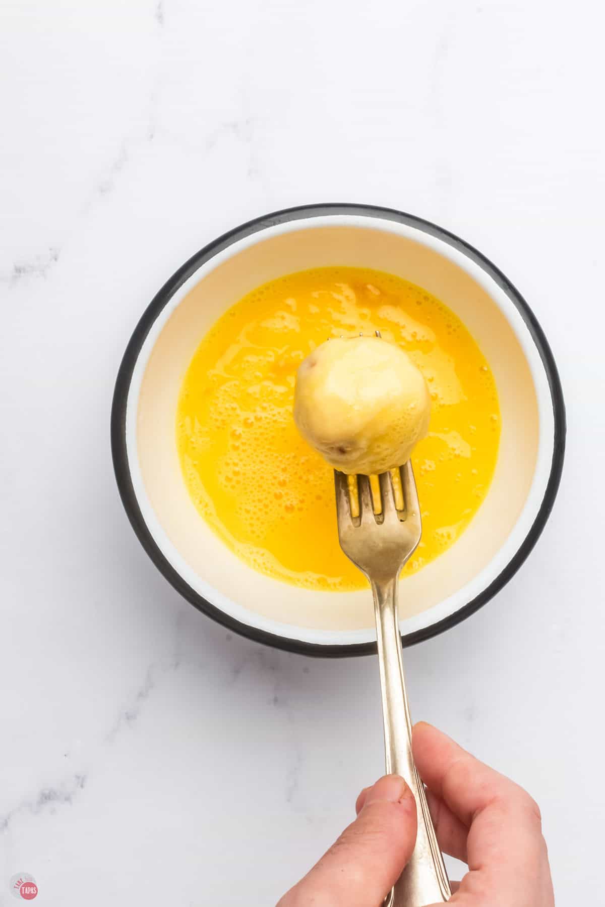 mashed potato ball on a fork being dipped in beaten egg