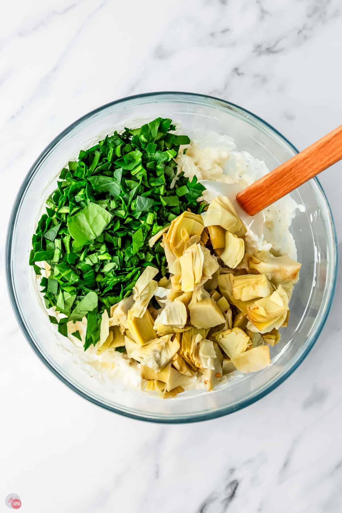 bowl of creamy dip with fresh spinach and artichoke hearts on top.