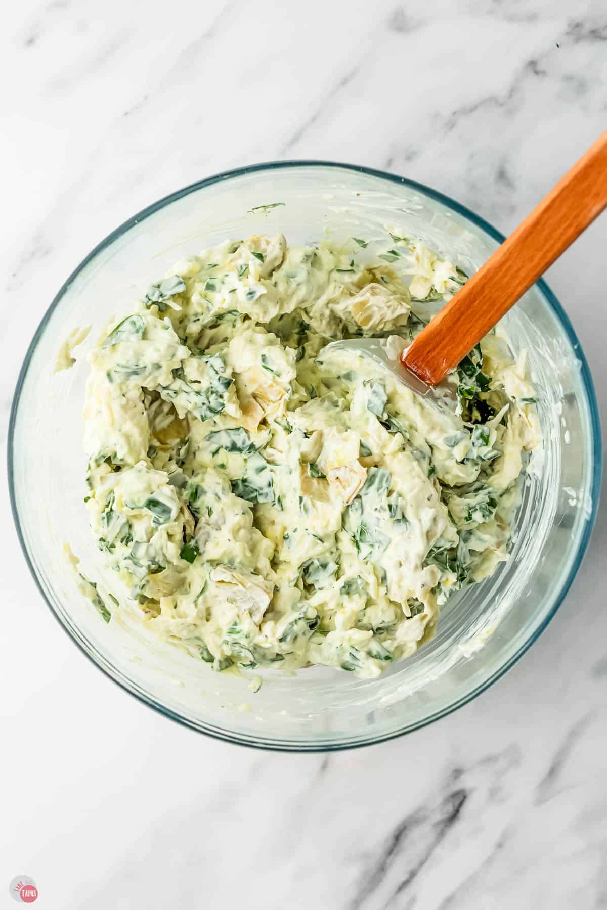 spinach artichoke dip in a clear bowl with a red spatula